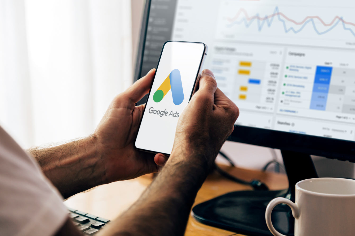 Google Ads logolu telefon ekranı ve arka planda Google Ads kampanya raporu