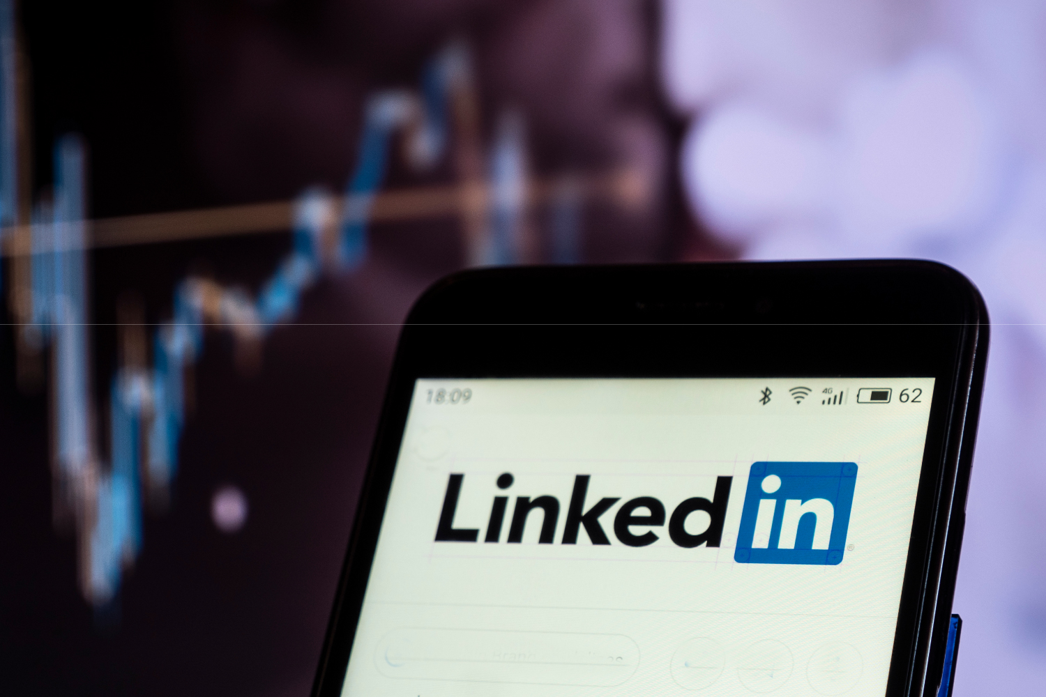 Yükselen veri grafiği önünde LinkedIn logosu görünen akıllı telefon