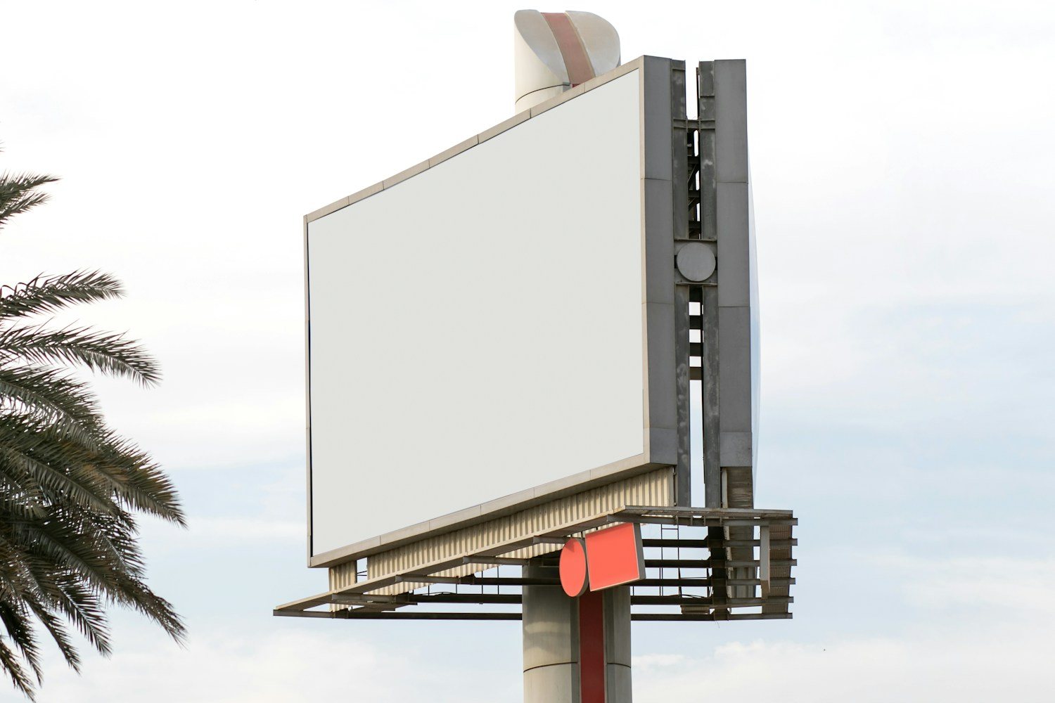 Palmiye ağacının yanında, bulutlu gökyüzüne karşı duran boş billboard