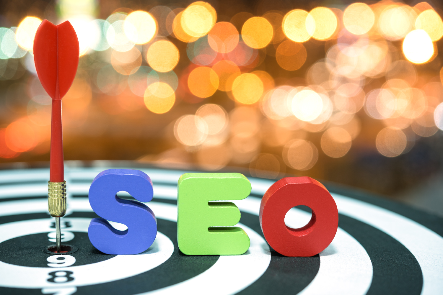 Dart tahtasının merkezine saplanmış ok ve renkli SEO harfleri