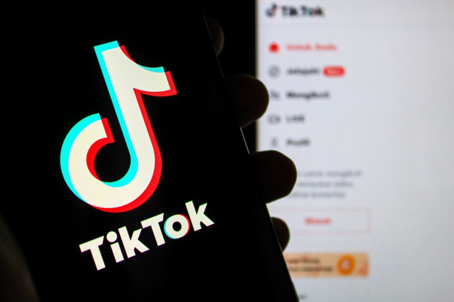 Elde tutulan telefon ekranında TikTok logosu ve arka planda bulanık TikTok menüsü