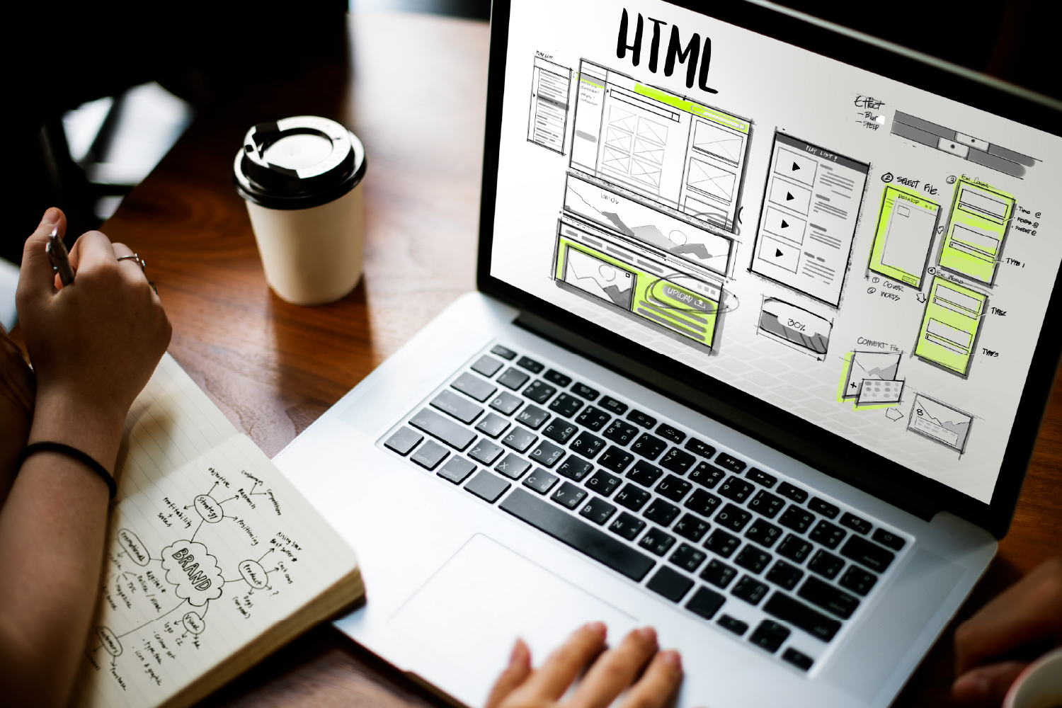 Dizüstü bilgisayar ekranında HTML web tasarım taslağı ve yanında not defteri