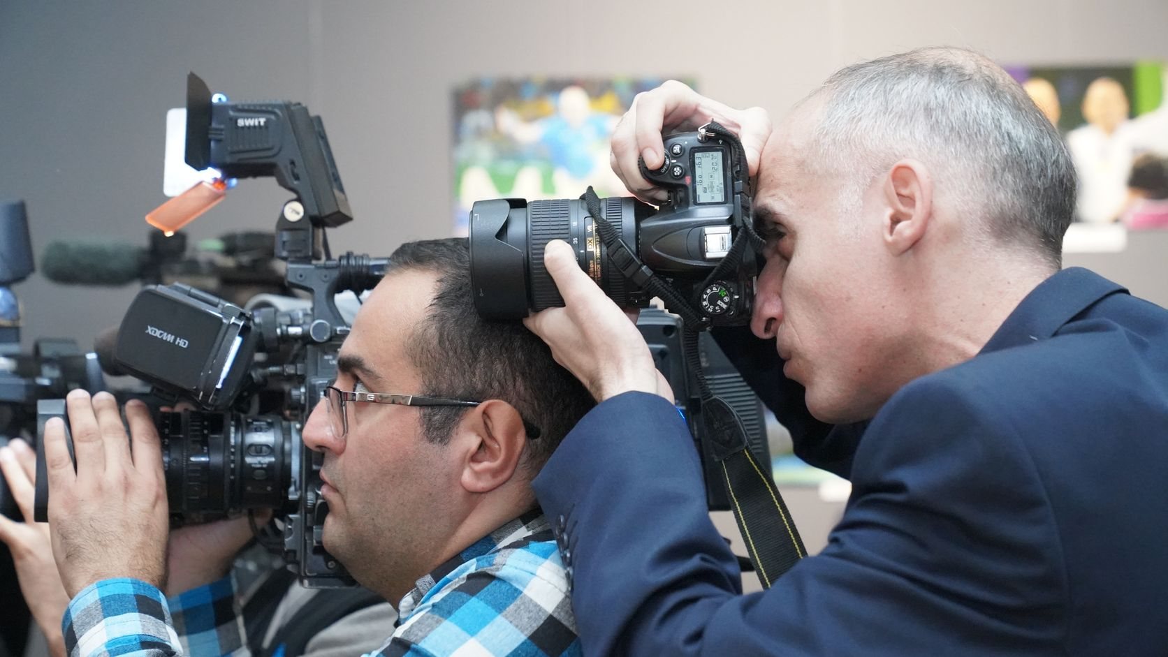 Etkinlikte omuz kamerası ve fotoğraf makinesiyle çekim yapan iki basın mensubu